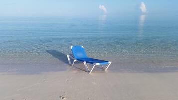 A beach with a single blue lounge chair on the sand.