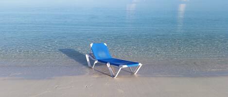 A beach with a single blue lounge chair on the sand.