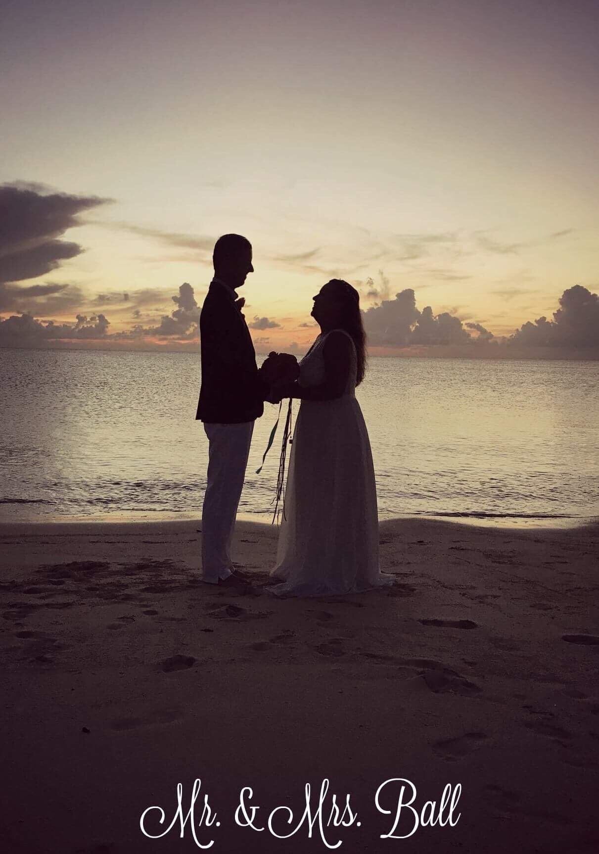 Una pareja parada en la playa con un atardecer de fondo.