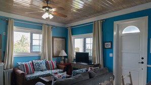 A living room with a blue wall, a ceiling fan, a sofa, a television, and a door. - Rollezz Villas Beach Resort (Old Bight)