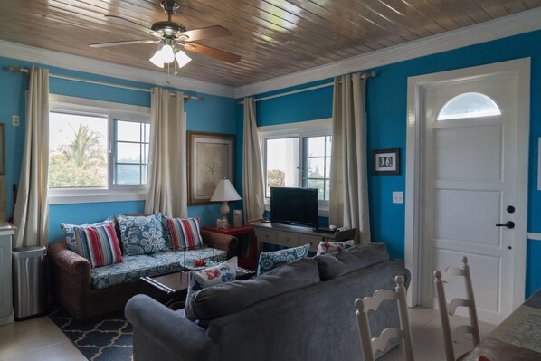 A living room with a blue wall, a ceiling fan, a sofa, a television, and a door.
