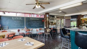 A cafeteria with tables and chairs, a chalkboard menu, and a clock on the wall.