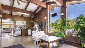A spacious room with a wooden ceiling, a large window with a view of the outside, a dining table, and a sofa.