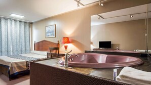 A hotel room with a bed, a bathroom with a bathtub, a mirror, and a television.