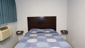 Una habitación de hotel con una cama, una mesita de noche, un control remoto y un aire acondicionado instalado en la pared.