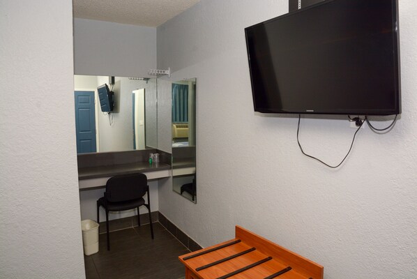A small room with a bed, a chair, a television mounted on the wall, and a mirror.