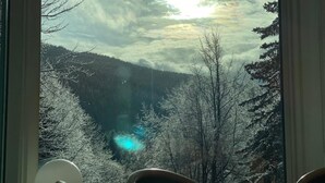 A room with a large window overlooking a forested valley, a wooden table, and a chair. - Interhotel Montana (Spindleruv Mlyn)