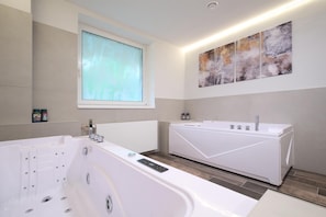 A modern bathroom with a large bathtub, a separate shower area, and a window providing natural light. - Interhotel Montana (Spindleruv Mlyn)