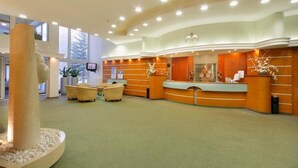 A reception area with a curved desk, seating, and a large pillar. - Interhotel Montana (Spindleruv Mlyn)