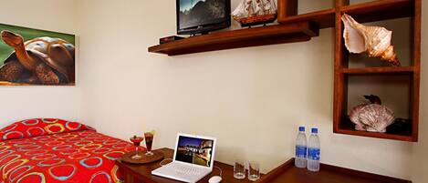 Habitación de hotel con cama, escritorio, computadora portátil, televisor y repisa con conchas marinas.