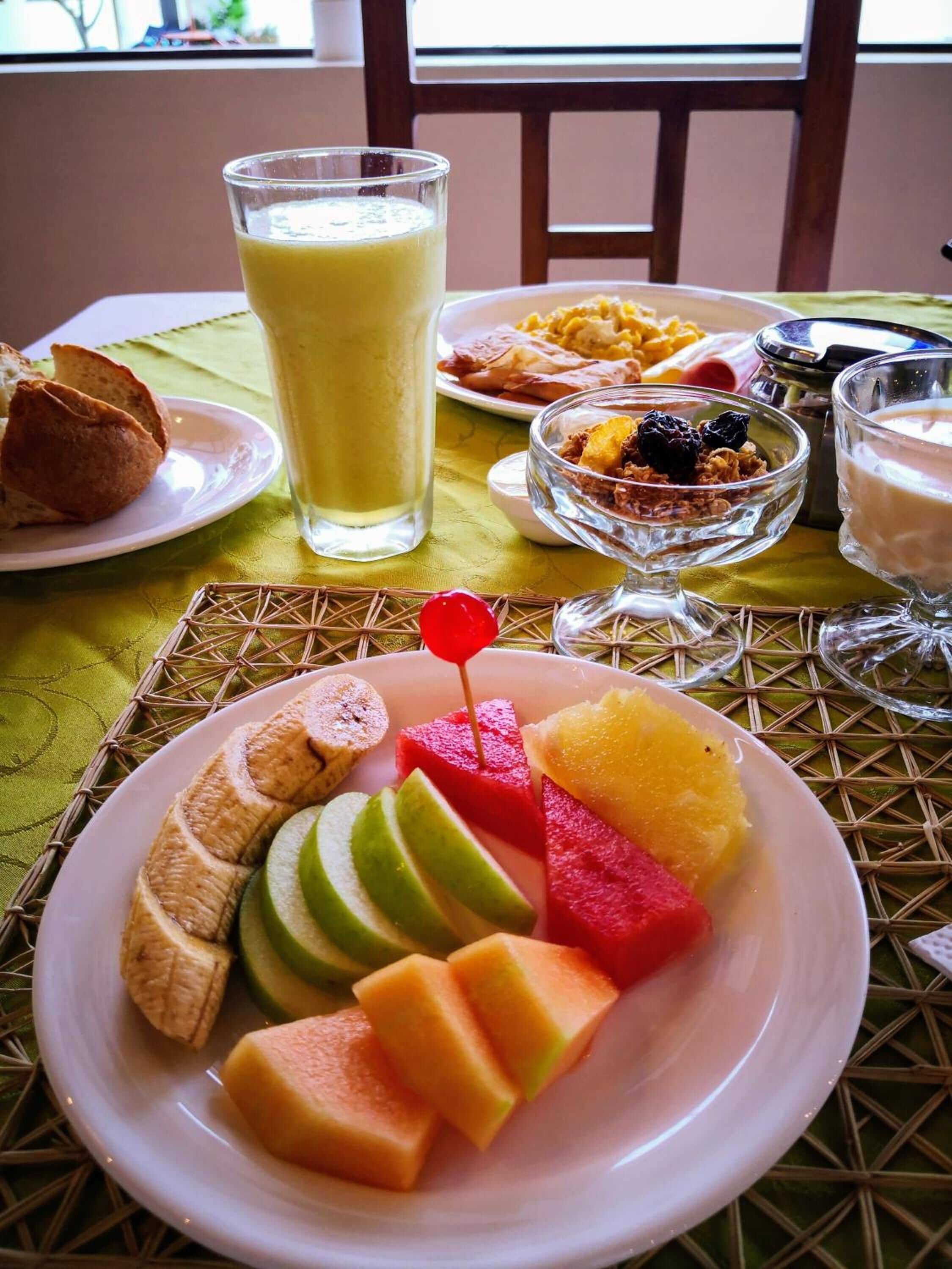 Una mesa con un plato de frutas cortadas, un vaso de jugo y un tazón de cereal.