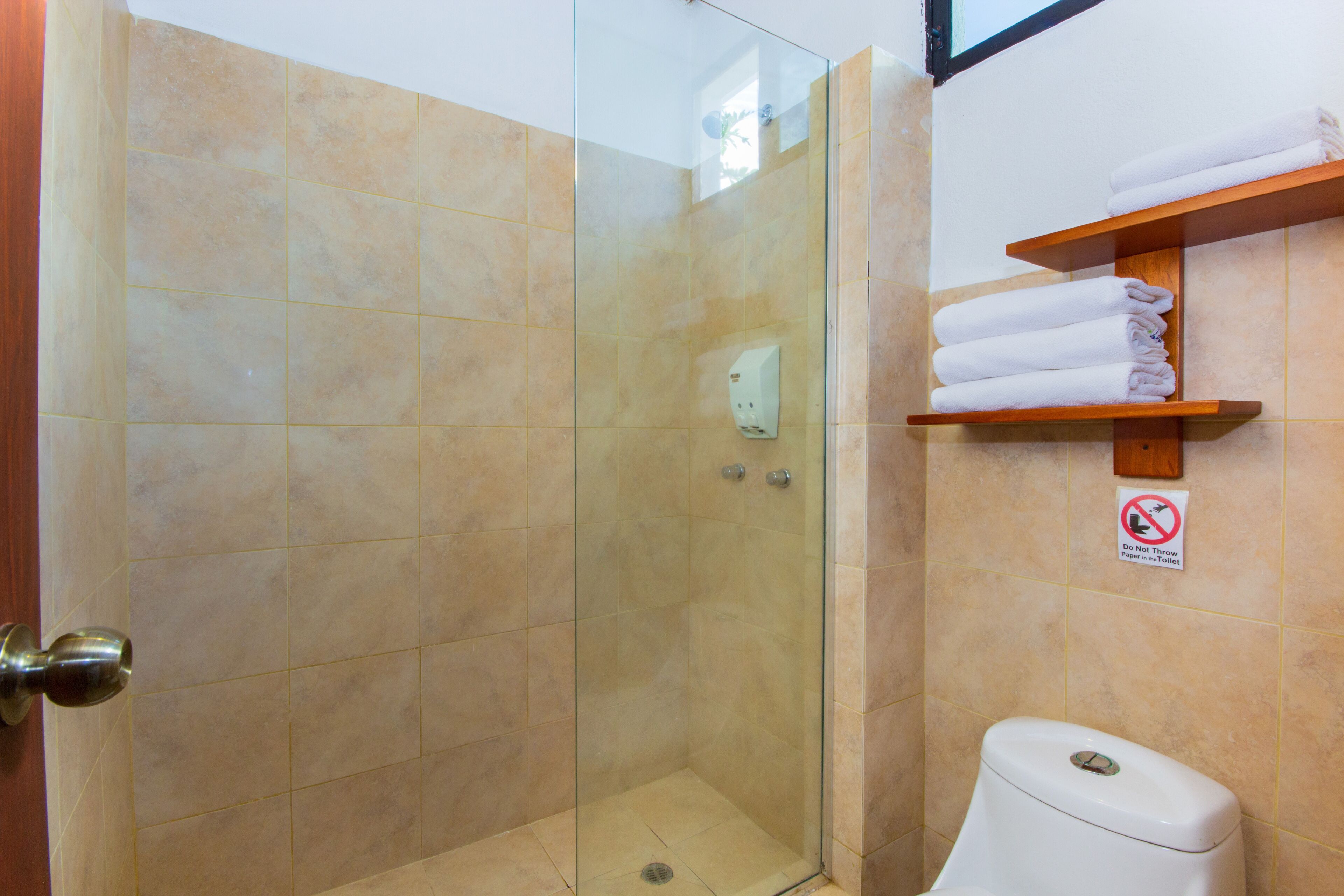 Un baño con cabina de ducha de vidrio, inodoro y repisa con toallas dobladas.