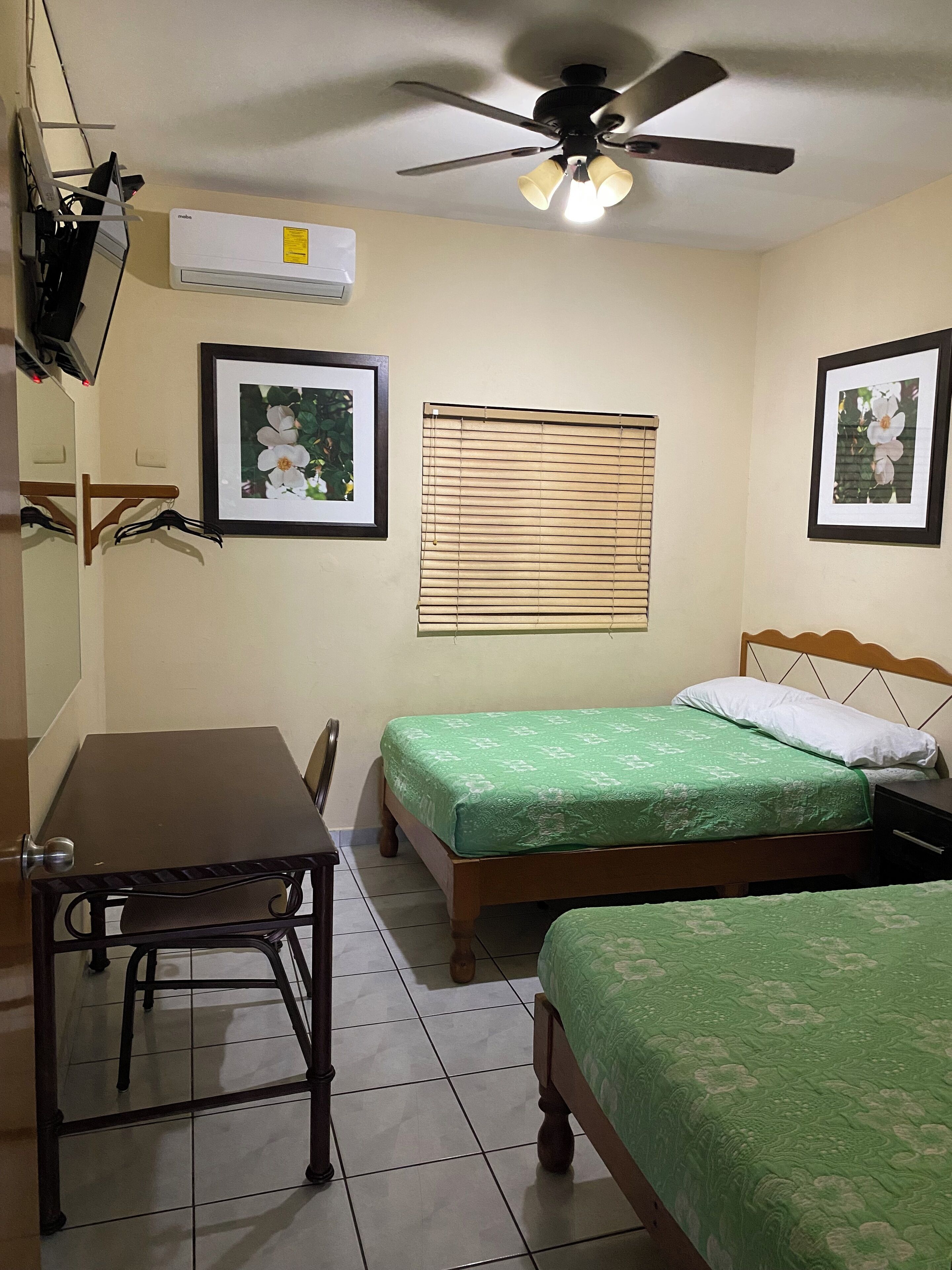 A bedroom with two beds, a ceiling fan, and framed pictures on the walls.