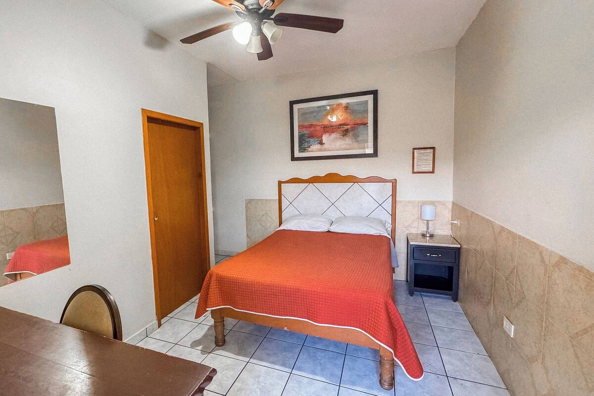 A bedroom with a bed, a ceiling fan, a nightstand, a chair, and a dining table.