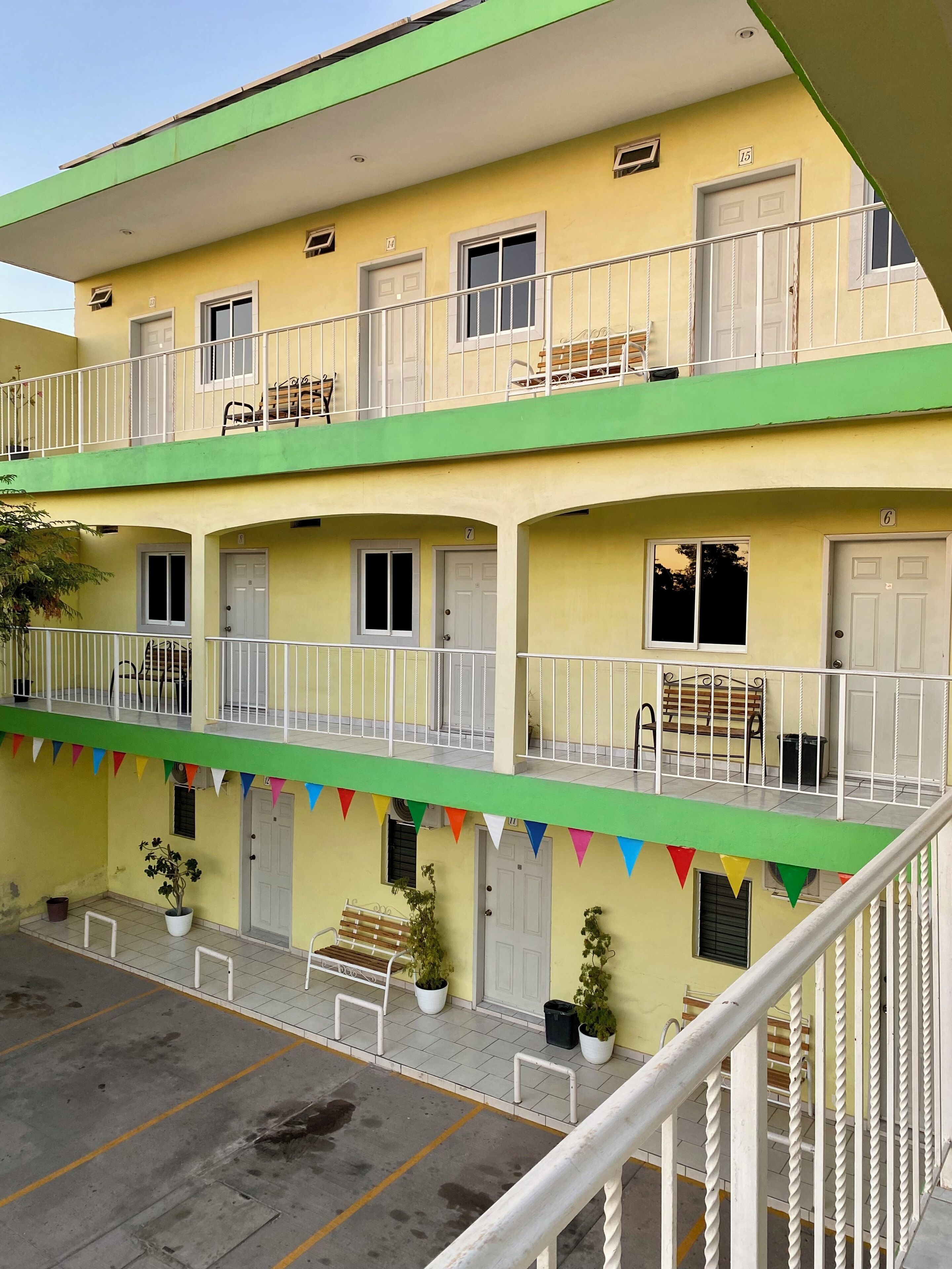 A two-story building with balconies, potted plants, and a bench.