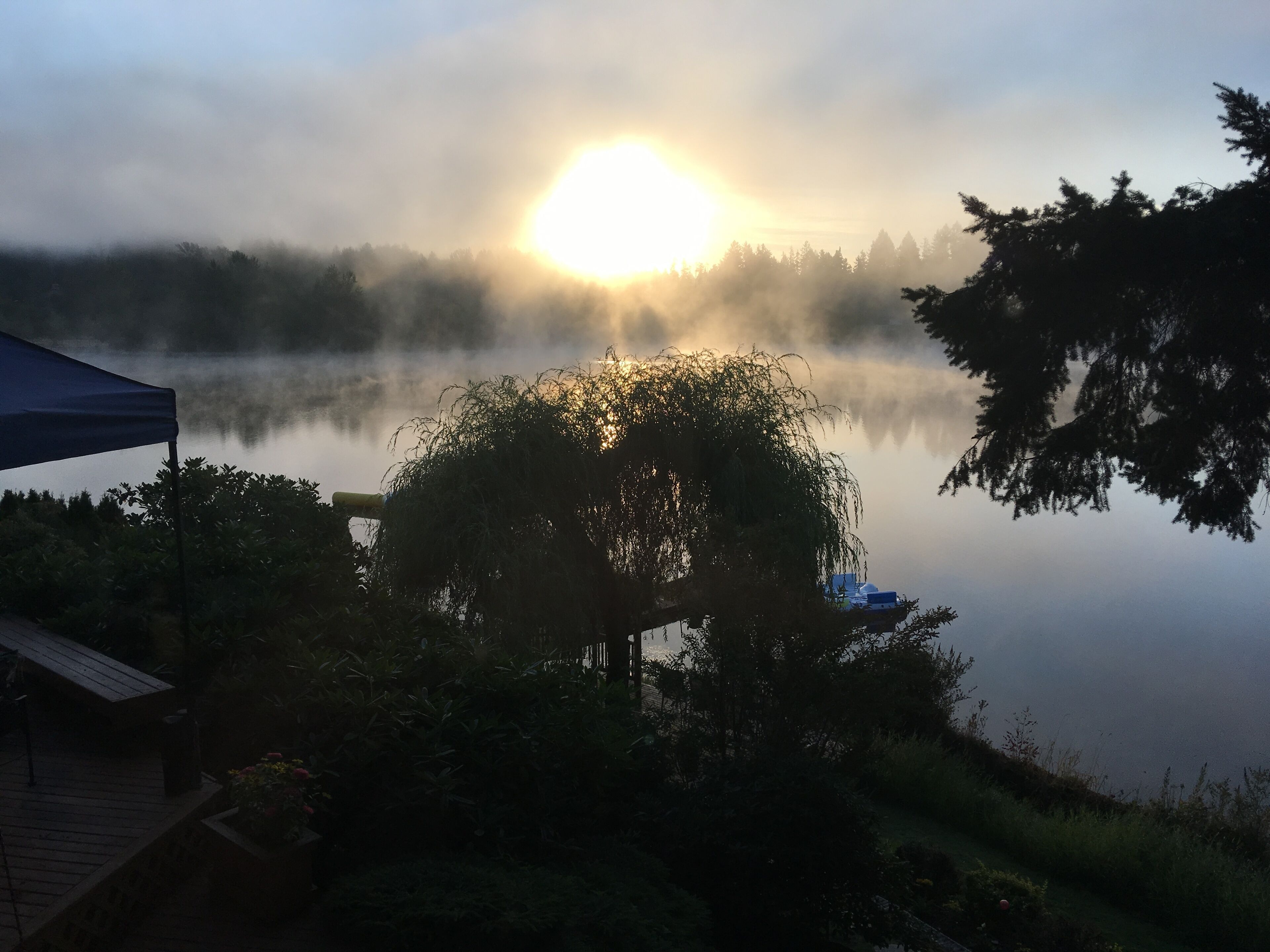 A serene lakeside view with a sunrise, a gazebo, and a house in the foreground.
