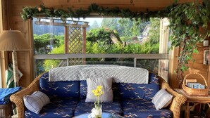 A cozy room with a wicker sofa, a glass coffee table, and a view of a lush garden through large windows. - Cottage Lake Bed and Breakfast (Woodinville)