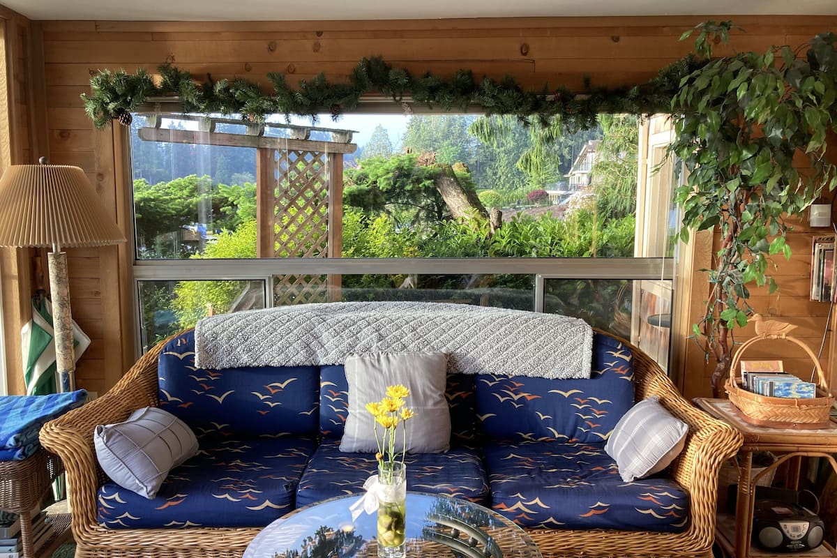 A cozy room with a wicker sofa, a glass coffee table, and a view of a lush garden through large windows.