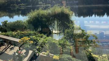 A wooden deck with potted plants and a view of a calm lake surrounded by trees.
