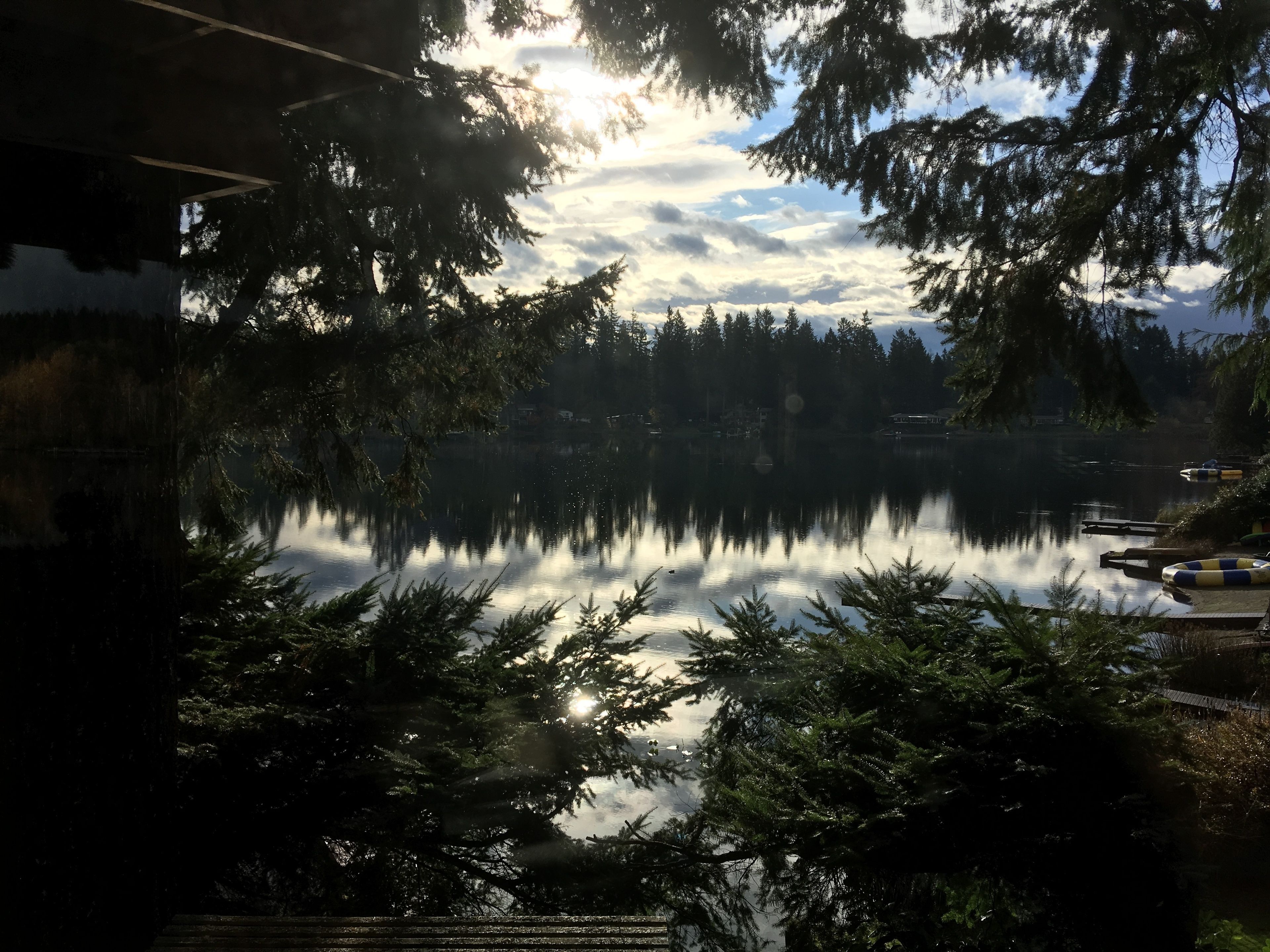 Ein ruhiger See, umgeben von dichtem Wald, mit deutlicher Spiegelung des Himmels und einigen Booten auf dem Wasser.
