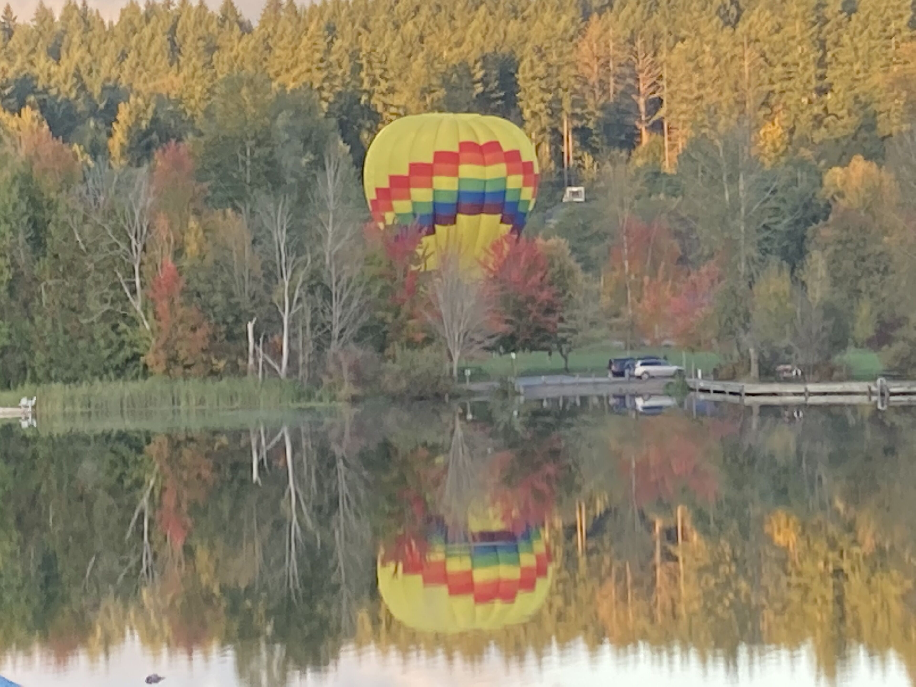 A hot air balloon over a lake with a forest in the background.