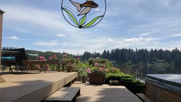 A wooden deck with benches, a hanging stained glass fish decoration, and a view of a lake and forested area.