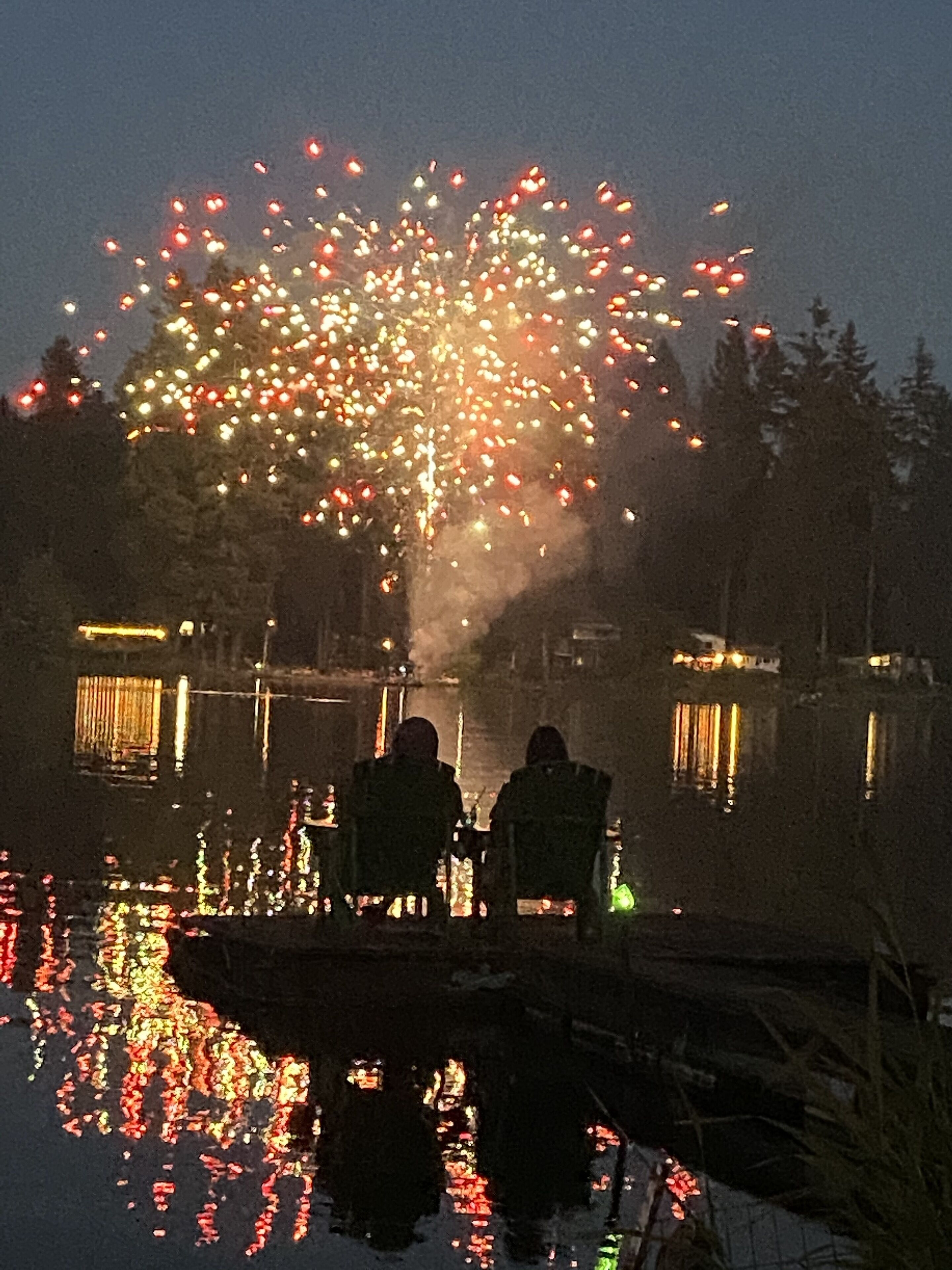 A nighttime scene with fireworks over a body of water, reflecting lights on the water's surface.