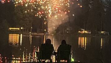 A nighttime scene with fireworks over a body of water, reflecting lights on the water's surface.