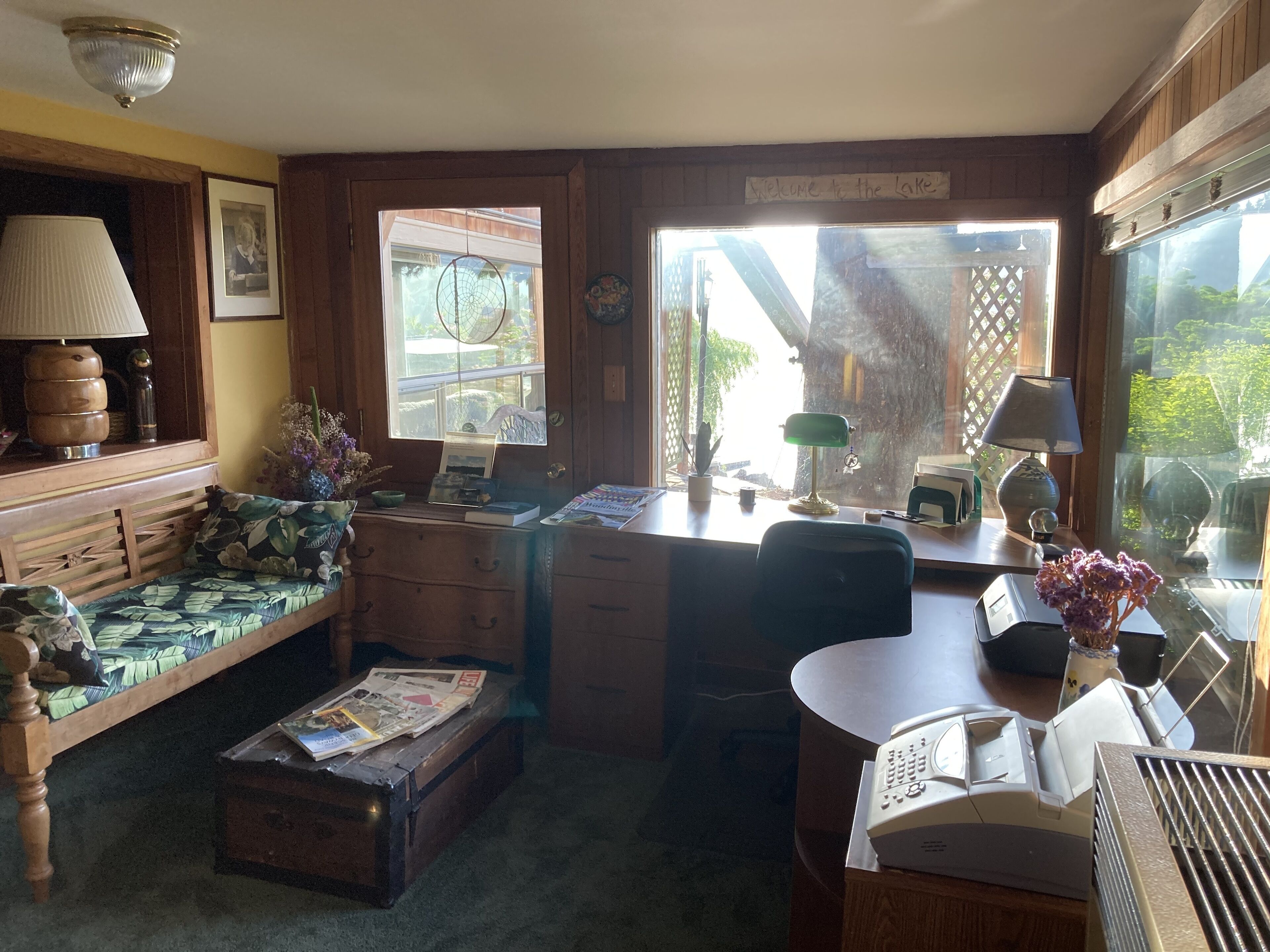A cozy room with a wooden desk, a comfortable chair, a sofa, and a window with a view of a bridge.