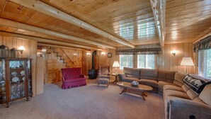 A cozy log cabin interior with a fireplace, plush seating, and a wooden staircase. - Grandma's Cabin (Island Park)