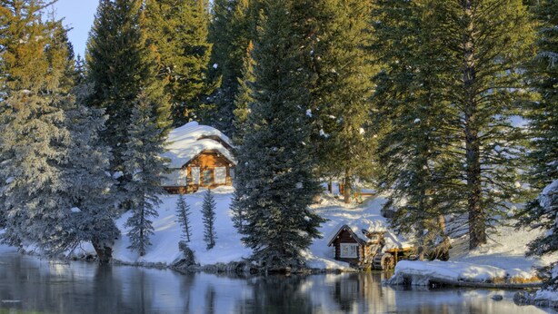 A cabin surrounded by snow-covered trees and a calm lake. - Grandma's Cabin (Island Park)