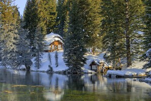 A cabin surrounded by snow-covered trees and a calm lake. - Grandma's Cabin (Island Park)