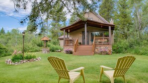 A cabin with a porch, two Adirondack chairs, and a stone wall. - Grandma's Cabin (Island Park)