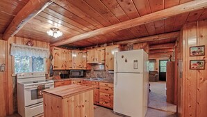 A wooden cabin kitchen with a stove, microwave, refrigerator, and wooden cabinets. - Grandma's Cabin (Island Park)