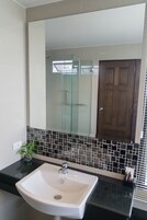 Un baño con un lavamanos blanco, cabina de ducha de vidrio y puerta de madera.