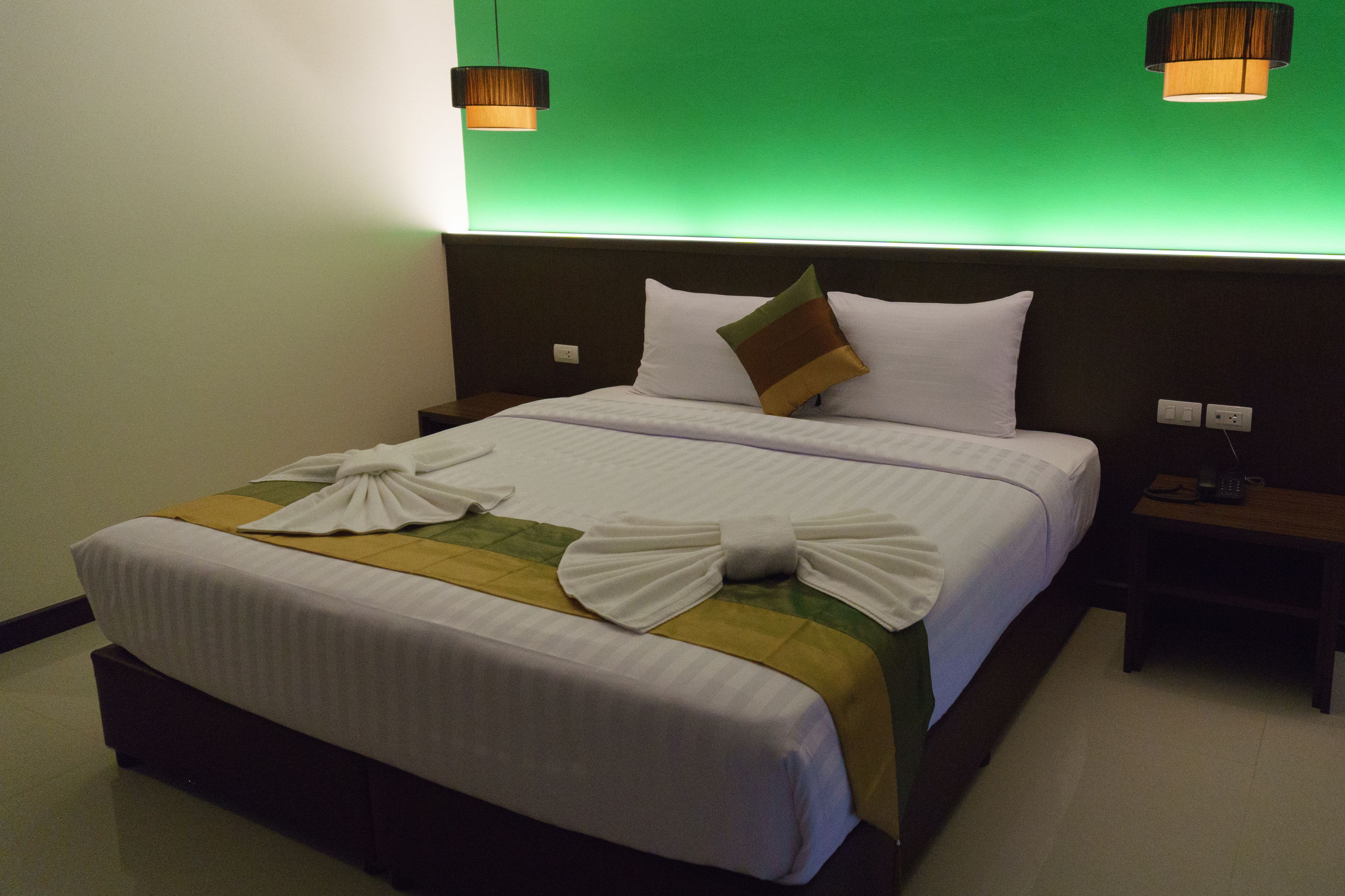 Una cama bien hecha con una pared verde y dos lámparas de pared.