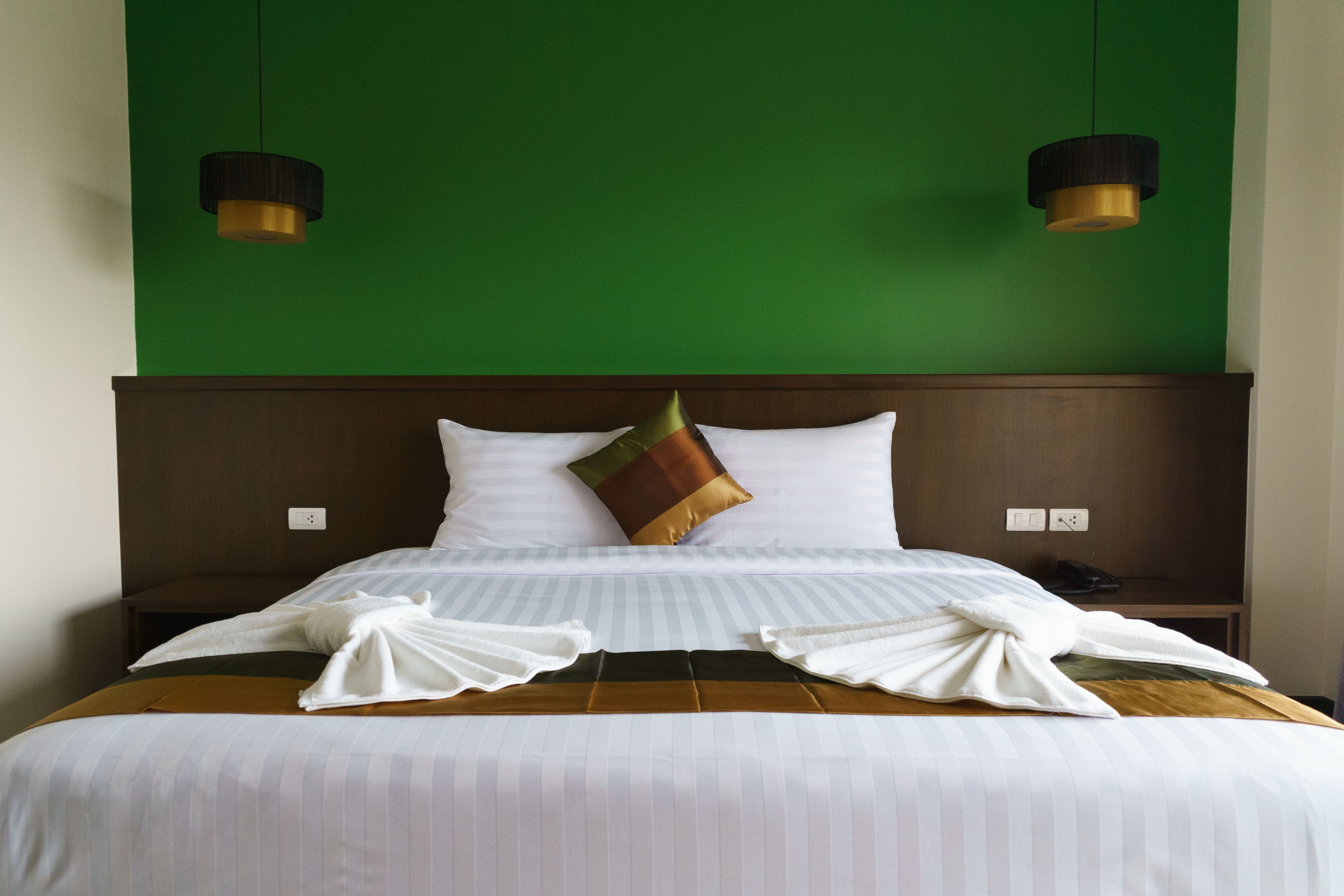 A neatly made bed with white linens and a brown headboard.