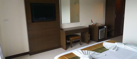 A hotel room with a bed, a desk, a mirror, and a minibar.