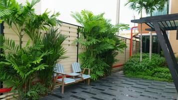 A patio area with two wooden chairs, a tiled floor, and lush green plants.