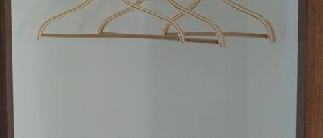 A room with a wardrobe containing a digital safe, a hanging rod with wooden hangers, and a door with a handle.
