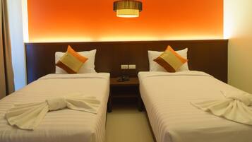 A hotel room with two beds, each with a pillow and a towel. There is a nightstand with a phone and a lamp between the beds.