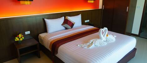 A hotel room with a large bed, a nightstand with a vase of flowers, and a red wall with a light strip.
