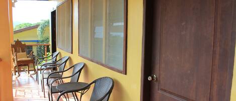 Un pasillo con sillas y mesas de mimbre, una puerta de madera y vistas al exterior con vegetación.