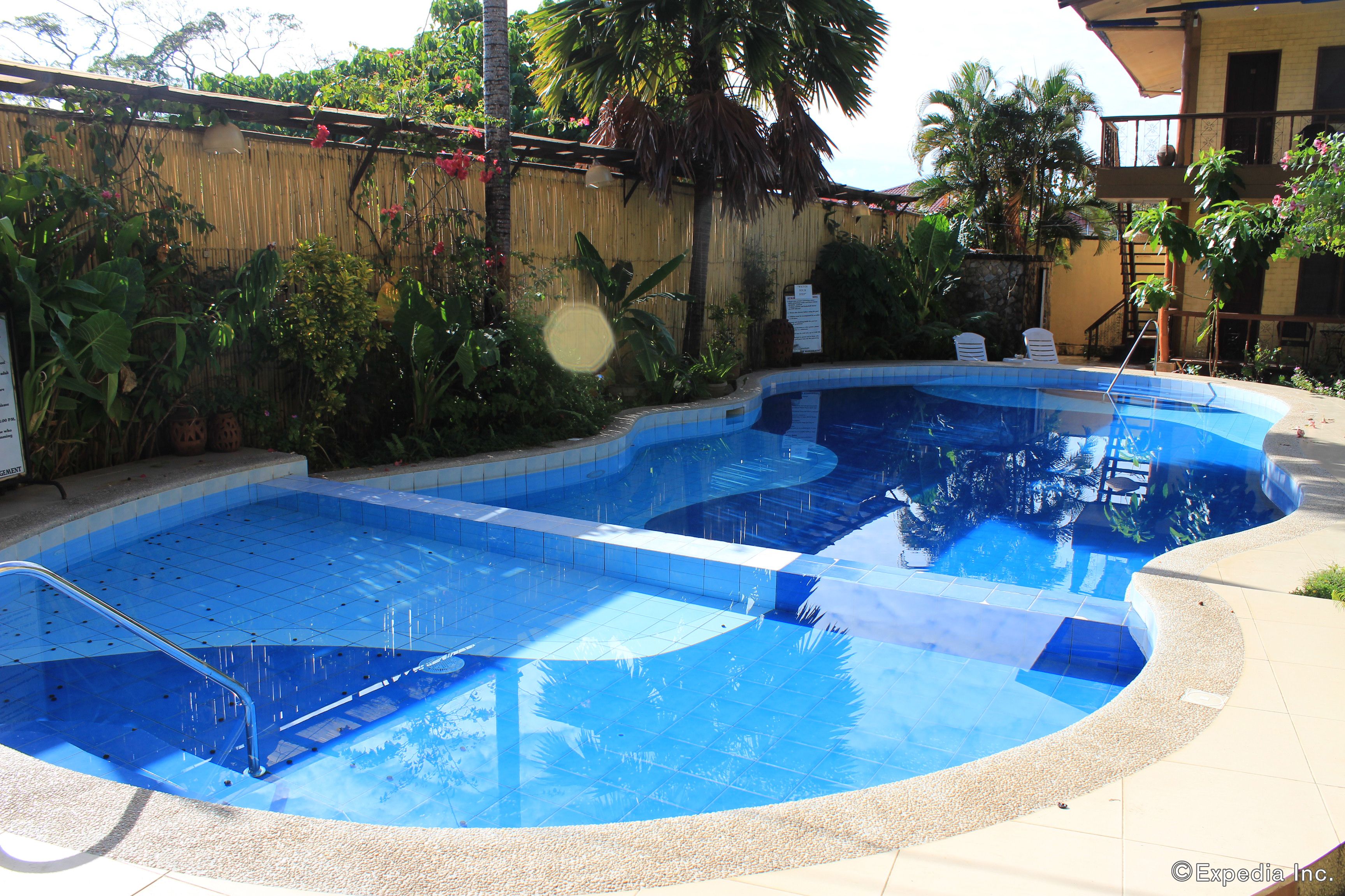 A swimming pool with a clear blue water, surrounded by a bamboo fence and tropical plants.