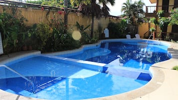 A swimming pool with a clear blue water, surrounded by a bamboo fence and tropical plants.