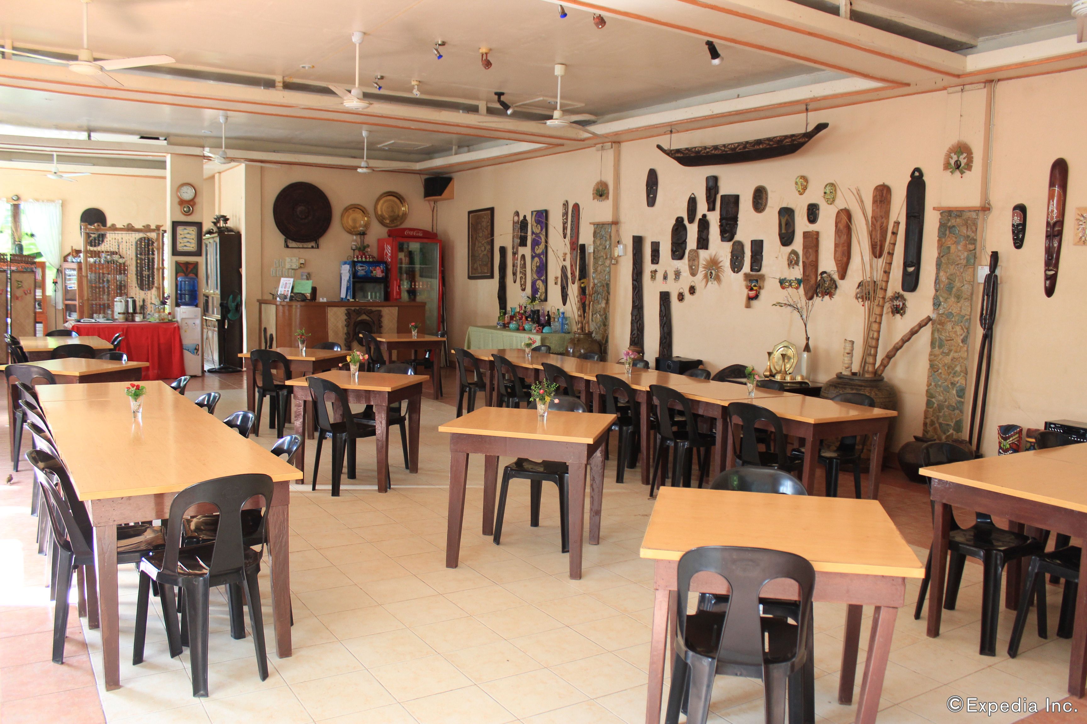 A dining area with multiple wooden tables and chairs, a red tablecloth on one table, and various decorative items on the walls.