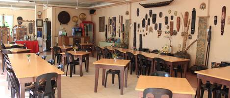 A dining area with multiple wooden tables and chairs, a red tablecloth on one table, and various decorative items on the walls.