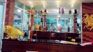 Uma área de bar com prateleiras de vidro exibindo diversos frascos, uma escultura dourada de peixe decorativo e uma parede de tijolos.