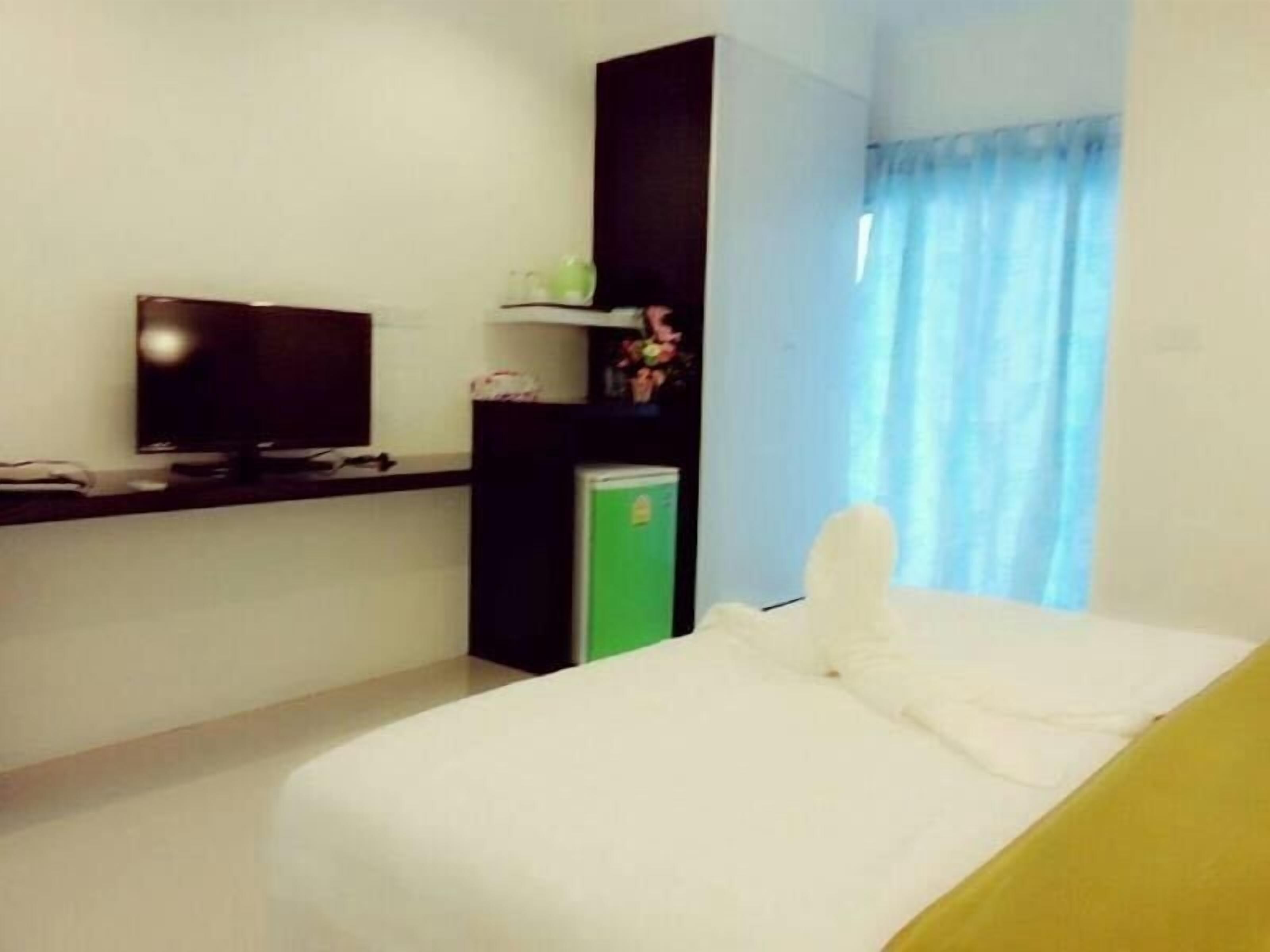 A hotel room with a bed, a TV, a small fridge, and a window with curtains.