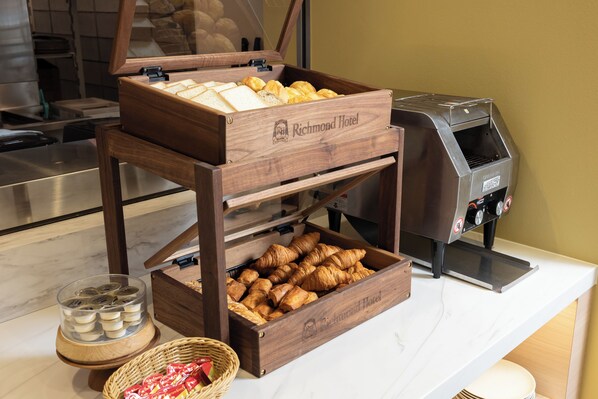 A breakfast buffet setup with bread, pastries, and a coffee machine at Richmond Hotel.